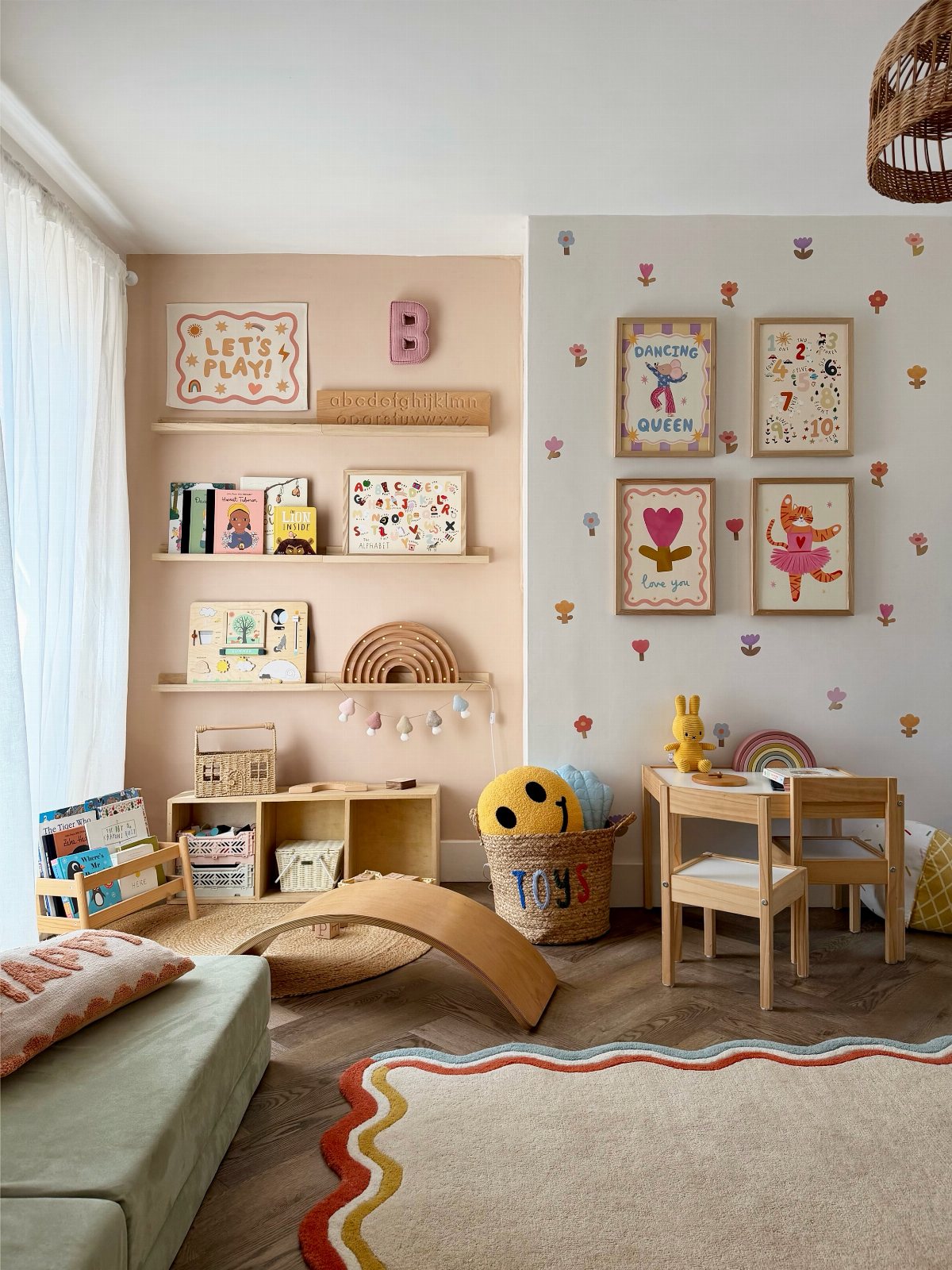 Children's playroom with wooden furniture, colorful wall decals, and framed art on shelves and walls.