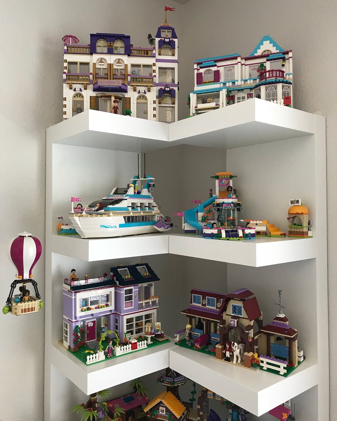 Large Lego building sets displayed on white corner floating shelves against a plain wall.