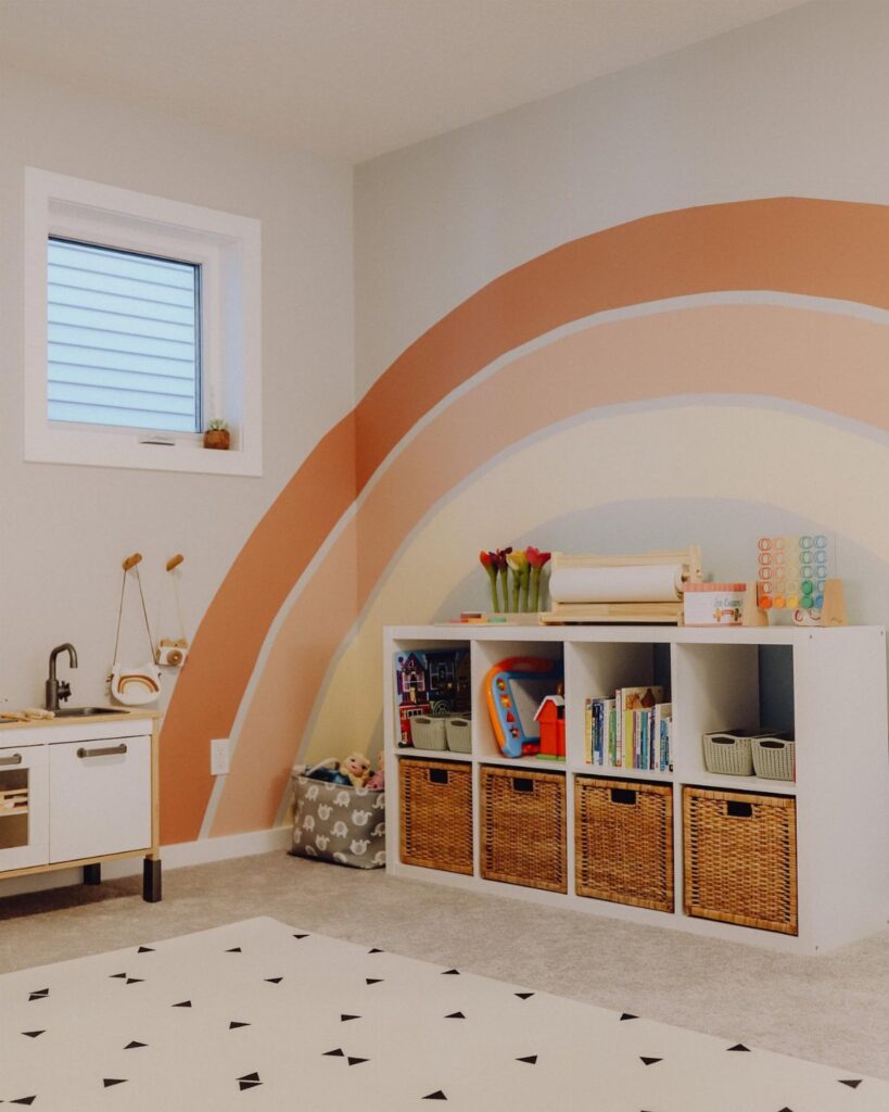 A playroom wall featuring a large painted rainbow mural above white storage cubbies with wicker baskets.