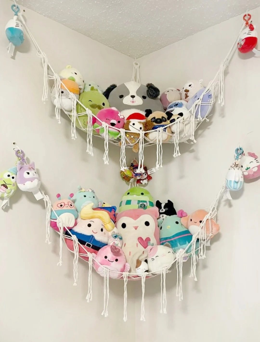 Two white macramé hammocks filled with colorful stuffed animals hanging in a room corner.