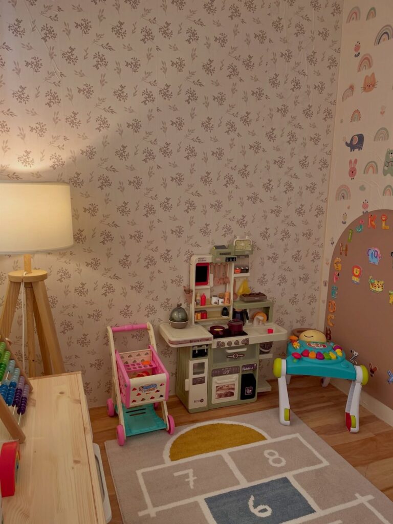 Toy kitchen, shopping cart, and activity walker on a hopscotch rug in a decorated playroom.