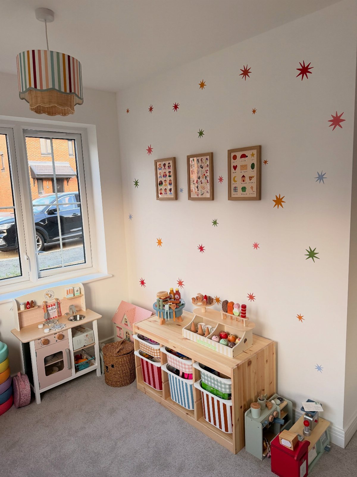 A small playroom featuring wooden toy storage, a play kitchen, and colorful star decals on white walls.