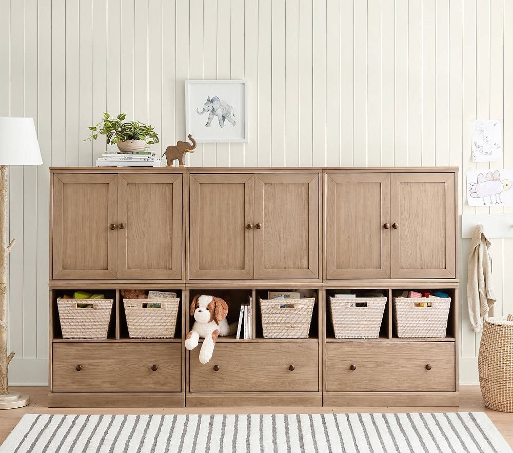 Wooden storage unit with cubbies containing woven baskets filled with toys and a stuffed animal.